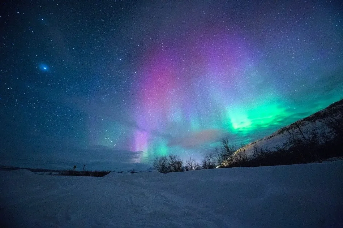 Colorful aurora borealis over snowy landscape at night.