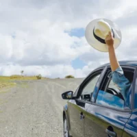 Person waving hat from car on rural road.