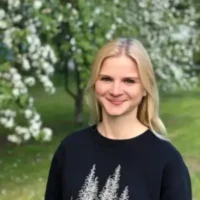 Smiling person outdoors with blossoming trees.