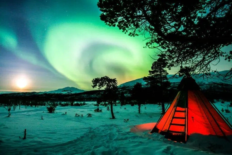 Northern lights over snowy landscape with glowing tent