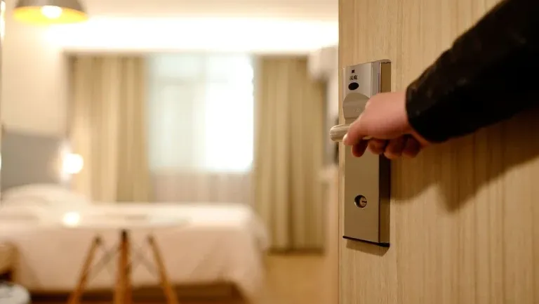 Hand opening hotel room door with bed inside