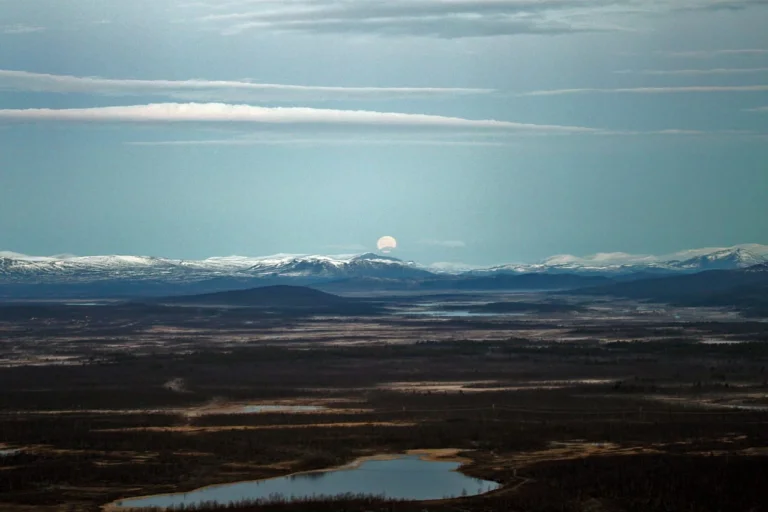 Moon rising over snow-capped mountain range and plains