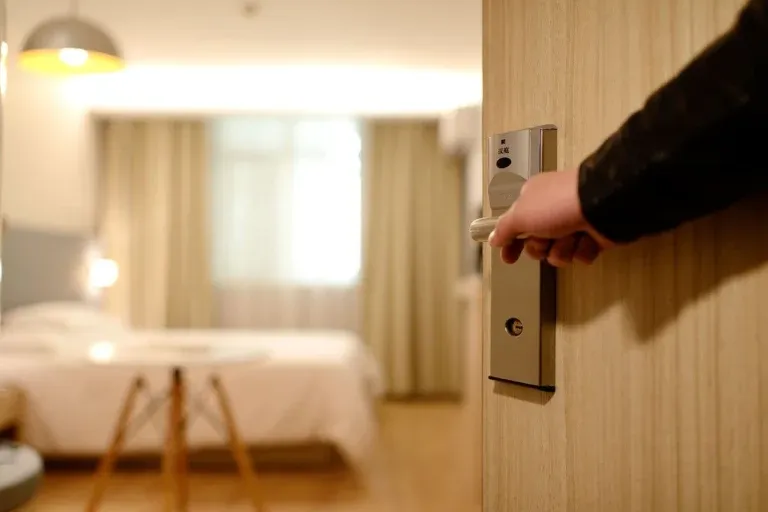 Hand opening hotel room door to bedroom