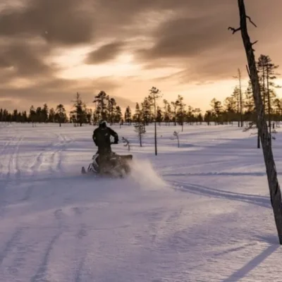 Person riding snowmobile across snowy landscape at sunset