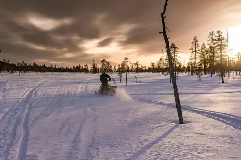 Snowmobile rider crossing snowy landscape at sunset