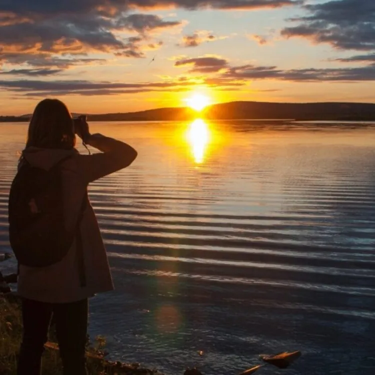 Person photographing sunset over calm lake