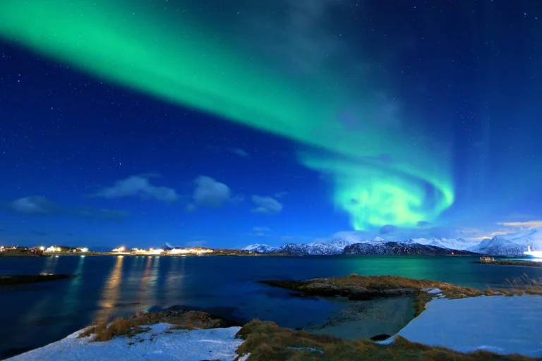 Northern lights over snowy coastal mountains at night