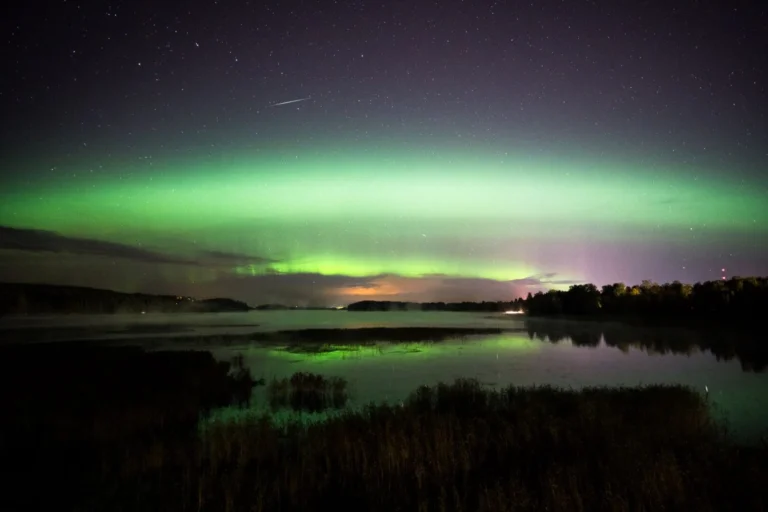 Green aurora over calm lake at night