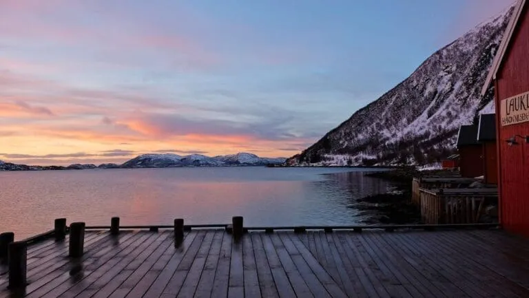 Snowy mountains and dock at sunset by fjord